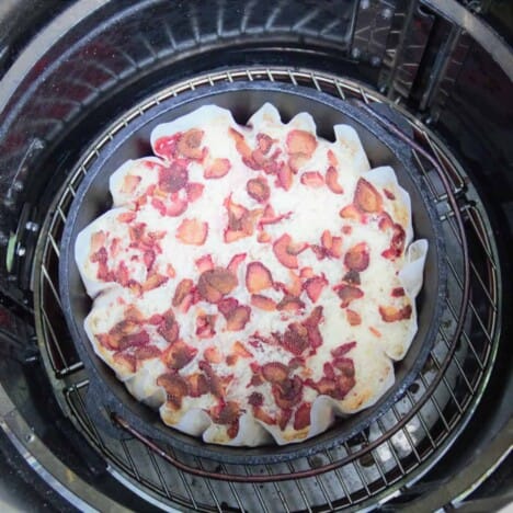 Looking down into a paper-lined Dutch oven on a grill grate, filled with strawberry dump cake batter.