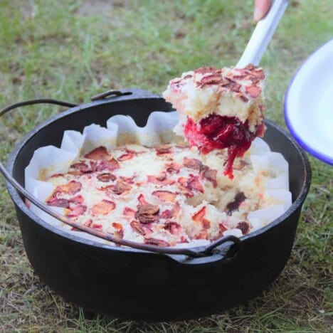 A spoonfull of the strawberry dump cake being served from a Dutch oven.