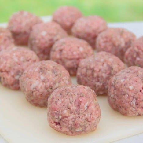 Chopping board covered in an even layer of round meatballs ready to be wrapped.