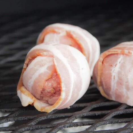 Close up of a raw Cheese Stuffed Bacon Wrapped Meatball added to a smoker rack.