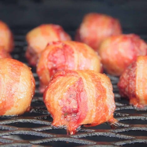 A few rows of cooked bacon wrapped cheese stuffed meatballs lay on a smoking rack.