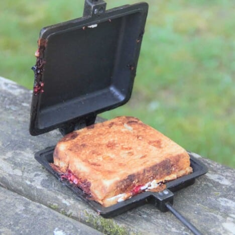 A golden brown toastie sits in a pie iron on a picnic table.