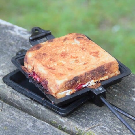 An open pie iron sitting on a picnic table with a chocolate, raspberry, and ricotta toastie.