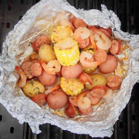 Looking down into a foil packet filled with shrimp, andouille sausage slices, baby red potatoes, and slices of corn.