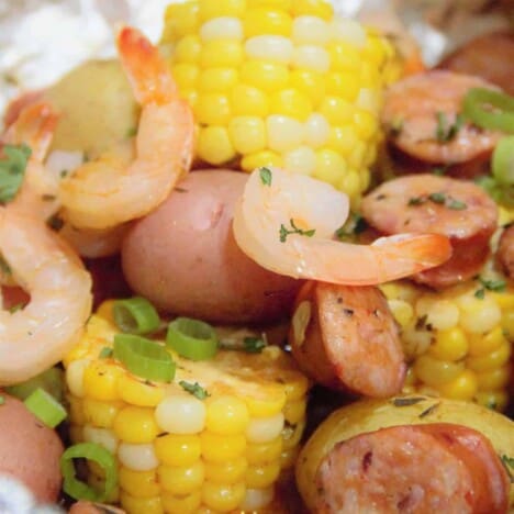 Large chunks of corn cobs are surrounded by cooked shrimp, andouille sausage, and baby red potatoes, sprinkled with chives.