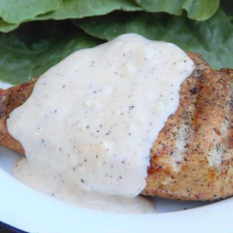 Alabama white sauce is poured over a piece of grilled chicken and green lettuce leaves in the background.