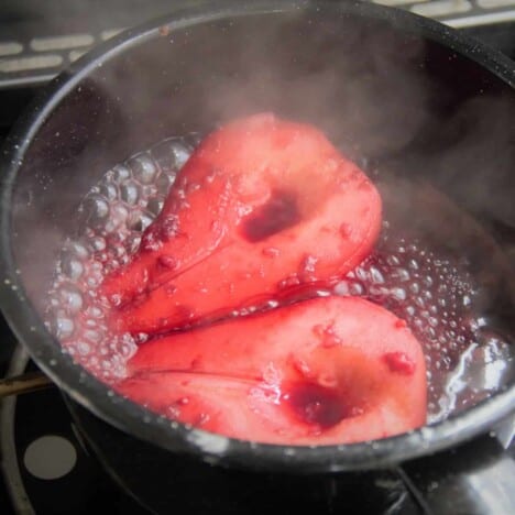 A black camp pot with two pear halves poaching in a red wine based liquid.