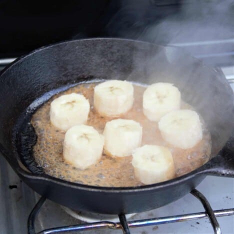 Raw banana slices just added to a hot butter and honey mixture in a cast iron skillet.