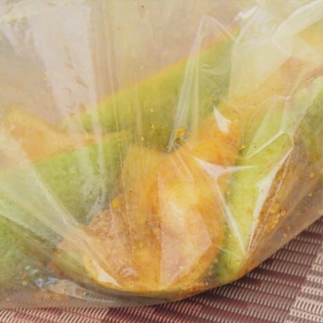 A plastic bag filled with pear quarters, sugar, and seasonings.
