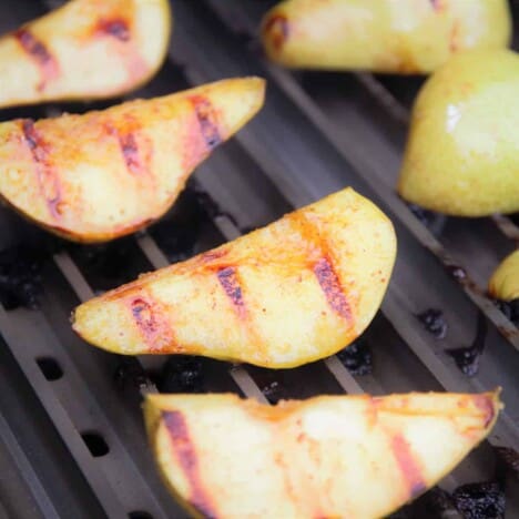 Grillgrates topped with well cooked pear quarters showing clear grill marks.