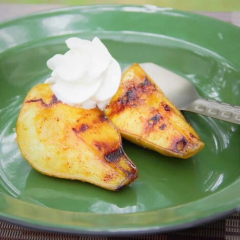 A green camp plate with two pieces of turmeric grilled pears and a side of whipped cream.