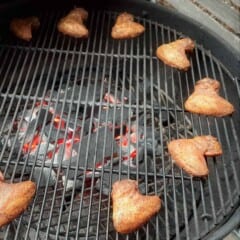 A circle of chicken wings cooks on a round grill.