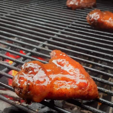A close up shot of a glazed chicken wing cooking over a grill grate.