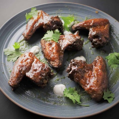Looking across a gray serving platter with glazed chicken wings sprinkled with cilantro leaves.