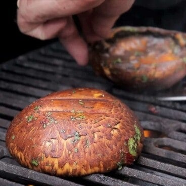 Two marinated portobello mushrooms are cooking on a grill grate.