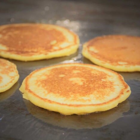 Four golden brown corn pancakes are cooking on a hot griddle.