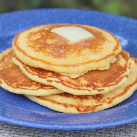 A stack of golden brown corn pancakes with a square of butter sit on top of a blue plate.