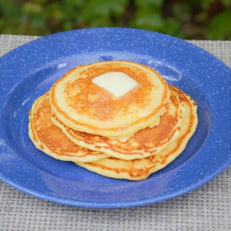 Looking down on a blue plate piled high with a stack of golden brown corn pancakes with a square of butter on top.