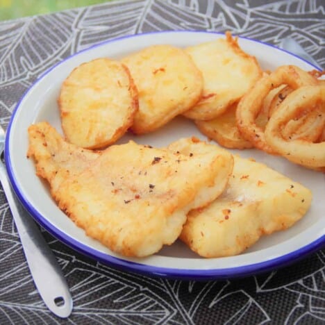 Beer batter fish rests on a white plate with a blue rim alongside fried onion rings.