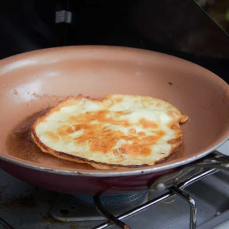 Looking down on a golden brown English pancake in a light brown skillet on a gas stove top.