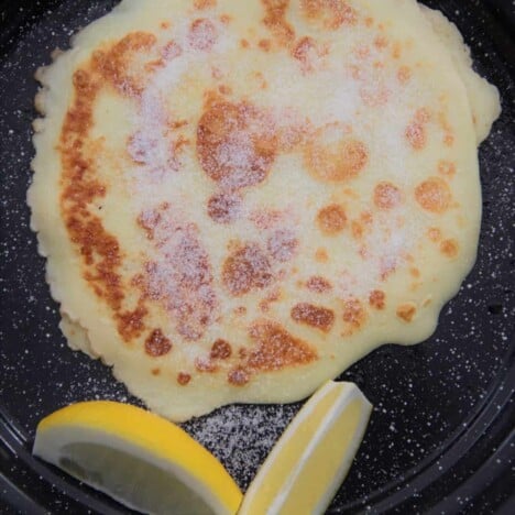 Looking down on a golden brown English pancake on a black tin plate with two lemon wedges on the side.