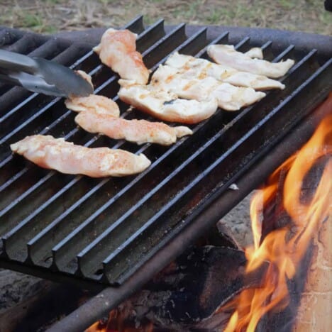 Seasoned and raw chicken tenders are being cooked on a hot grill grate.