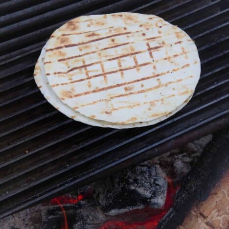 A flour tortilla with grill hatch marks sits on a hot grill grate.