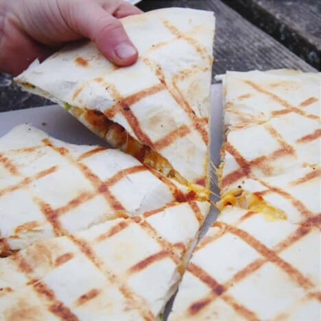 A white hand is removing a grilled quesadilla wedge from a whole quesadilla.