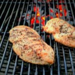 Two seasoned chicken breasts, with nice dark grill marks, sit on a hot grill.