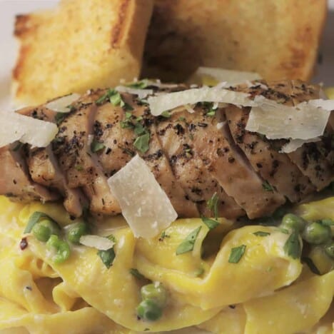 Sliced grilled chicken sprinkled with Parmesan cheese sits between fresh noodles and toasted baguette.