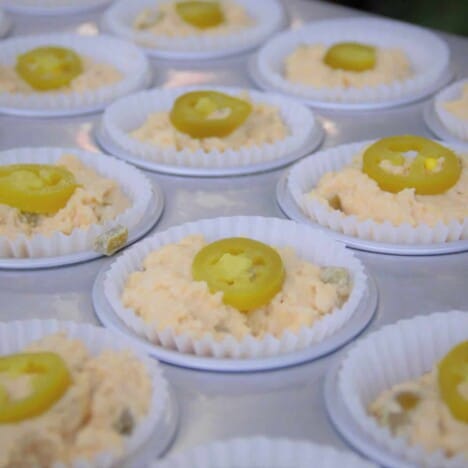 An angled shot of several muffin cups filled with cornbread muffin batter, topped with a slice of jalapeno.