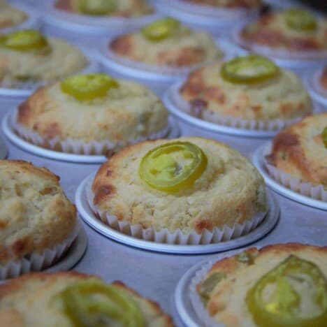 A row of jalapeno cornbread muffins with slices of jalapeno on top that are almost golden brown.