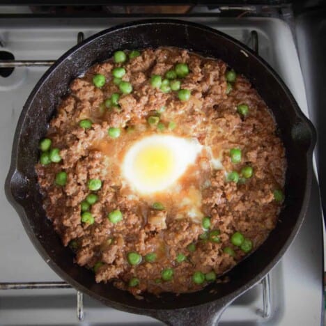 Looking down on a skillet filled with a meat and pea stew with an egg in the middle.