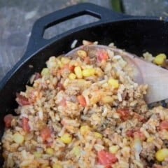 Looking down into a cast iron skillet filled with rice, corn, and tomatoes being stirred with a wooden spoon.