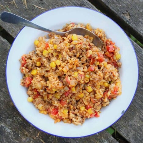 Looking down into a shallow white bowl filled with rice, tomatoes, and corn on a wood picnic table background.