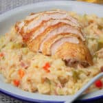 A plate of Cajun style risotto with a sliced breast of smoked chicken layered on top.