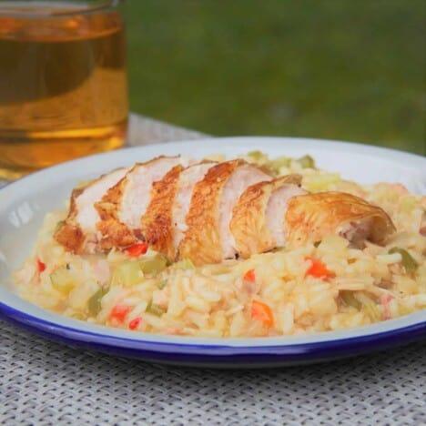 Looking across a white plate filled with Cajun style risotto with a sliced smoked chicken breast layered on top, and a green background.