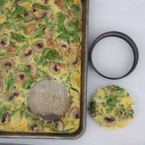 Looking down on to a baking pan filled with a cooked spinach and mushroom omelette with a round piece cut out and set on a white background.