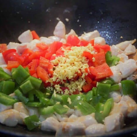 Looking into a wok with chunks of chicken, green and red bell peppers, and minced garlic.