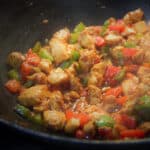 Looking into a dark wok with cooked stir fried chicken and bell peppers in sauce.