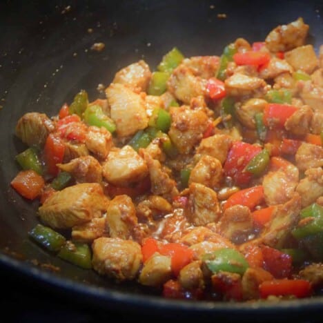 Looking into a dark wok with cooked stir fried chicken and bell peppers in sauce.