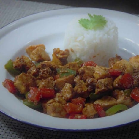 Looking across a white deep dish plate holding stir fried chicken with bell peppers and a serving of white rice.