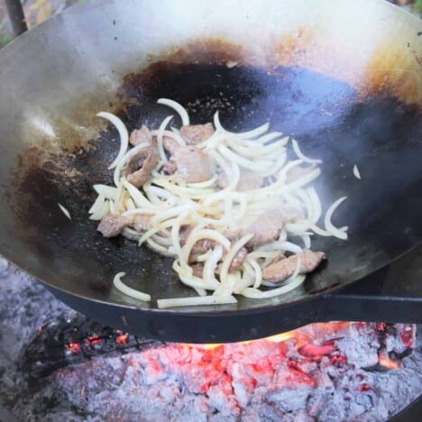 Sliced raw yellow onions are sauteed with beef in a wok over hot coals.