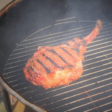 A single tomahawk steak with dark char marks is cooking on a small grill.