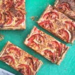 Five slices of tomato and pesto tart sit on a teal background.