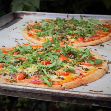 Two baked bacon, tomato, and arugula pizzas on a baking sheet lined with parchment paper.