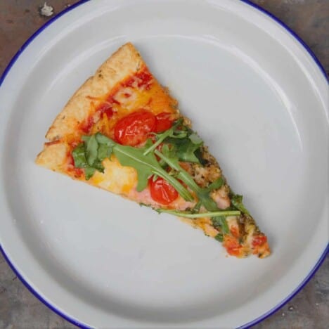 A single slice of bacon, tomato, and arugula pizza on a white plate.