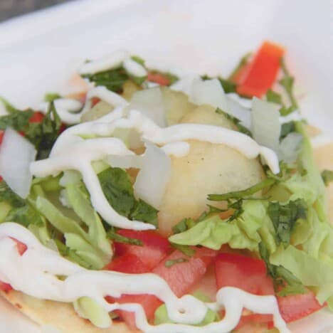 A closeup shot of a walleye fish taco with fried fish pieces, tomatoes, cilantro, and a drizzle of sauce.