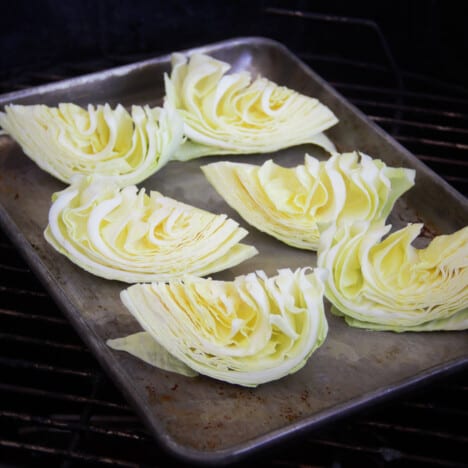 Six wedges of green cabbage are sitting on a baking sheet on top of a grill grate.