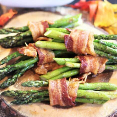 Looking down on to several bundles of bacon-wrapped asparagus spears, resting on a wooden plate.